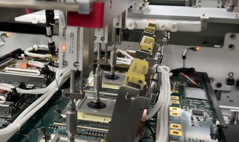 An industrial assembly machine with multiple robotic heads lowering suction nozzles onto a green printed circuit board.