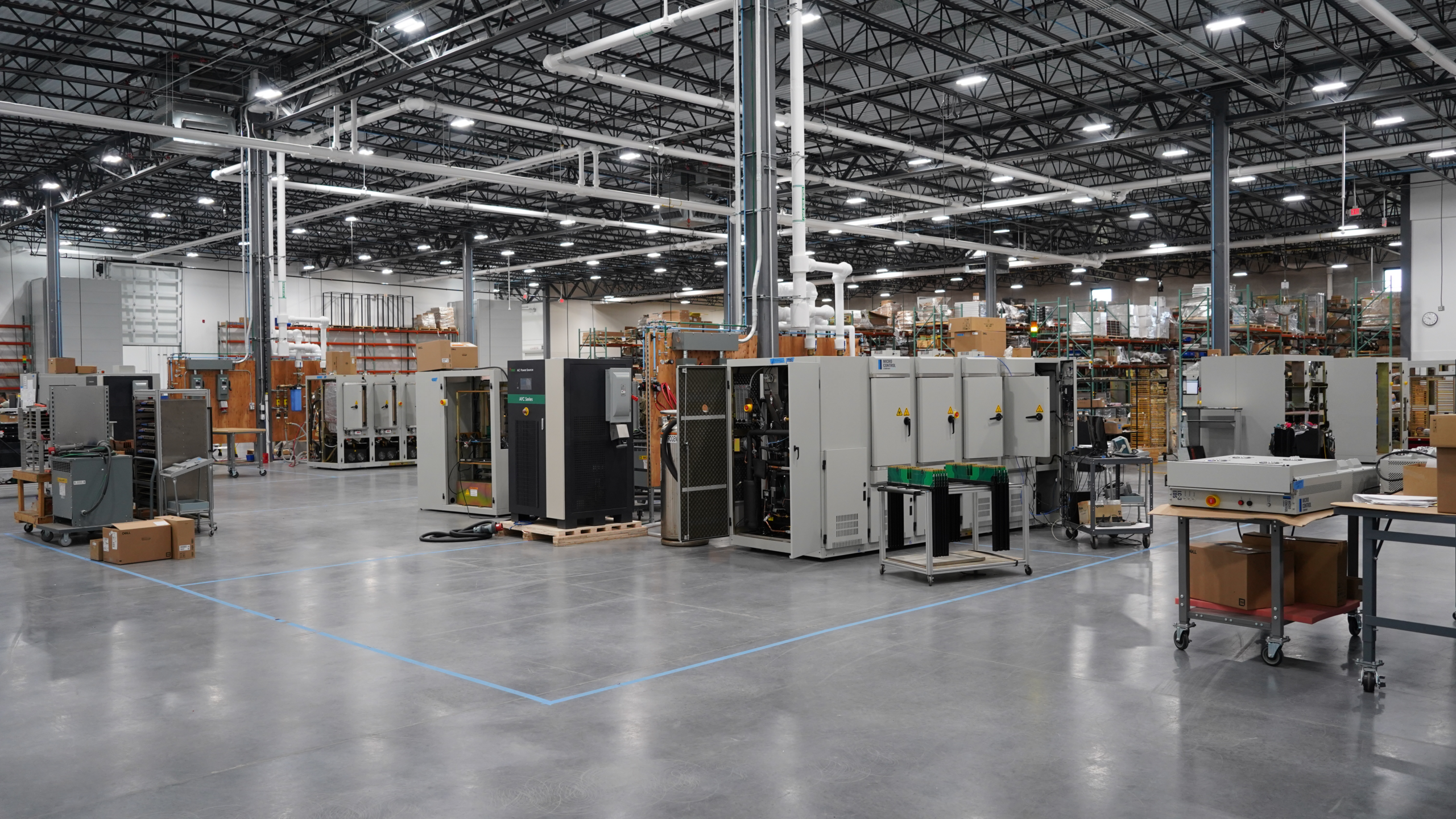 A large industrial warehouse floor filled with rows of metal equipment cabinets and work carts.