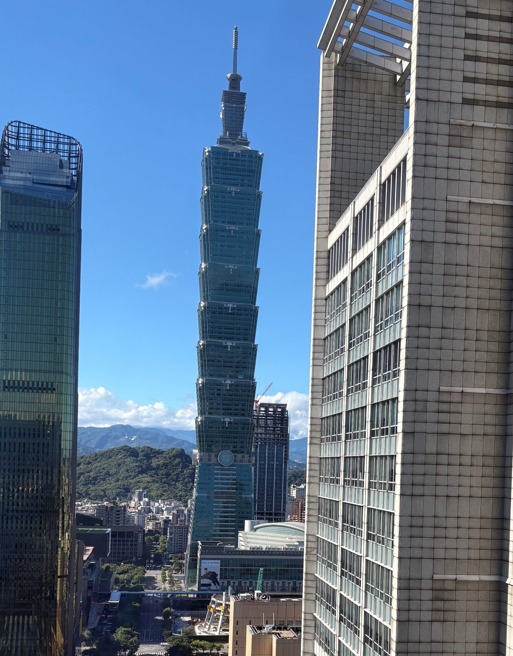 Taipei 101 skyscraper rising above the city, framed by two tall modern buildings under a clear blue sky.