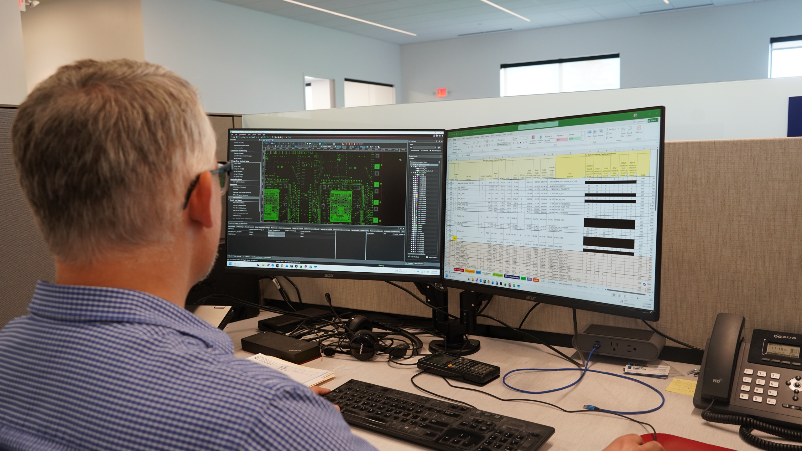 A man sitting at a desk looking at two computer monitors displaying technical software and a spreadsheet.