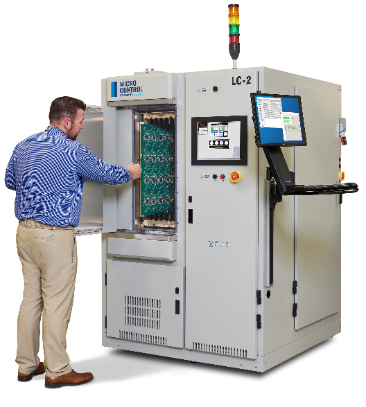 A technician places a green circuit board into a Micro Control LC-2 testing machine.