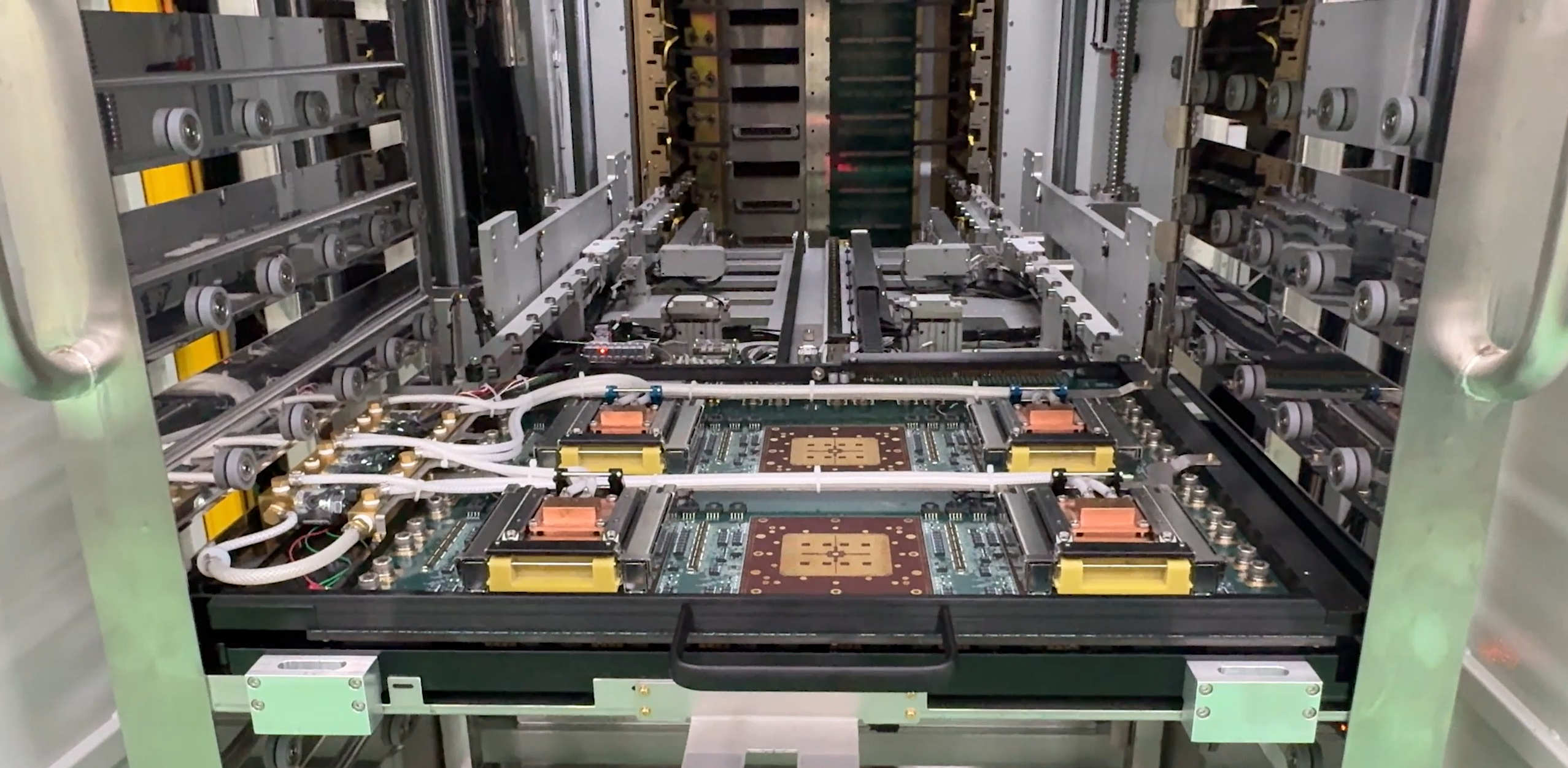 Interior view of an industrial automated machine featuring four square circuit board modules connected by white tubing and mounted on a sliding track system.